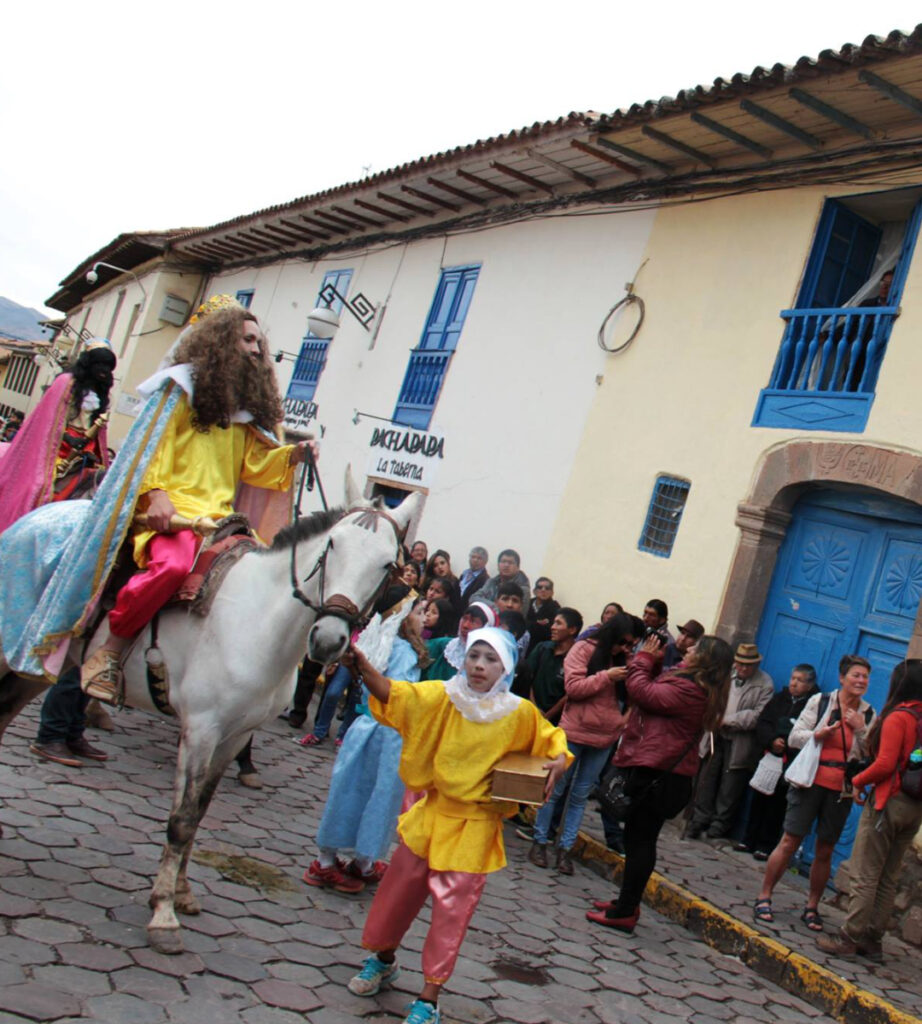 Procissão da Baixada de Reis no bairro de San Blas em Cusco, com personagens tradicionais desfilando pelas ruas de pedra, fiéis assistindo à celebração e casas coloniais ao fundo, festa cultural de janeiro no Peru.