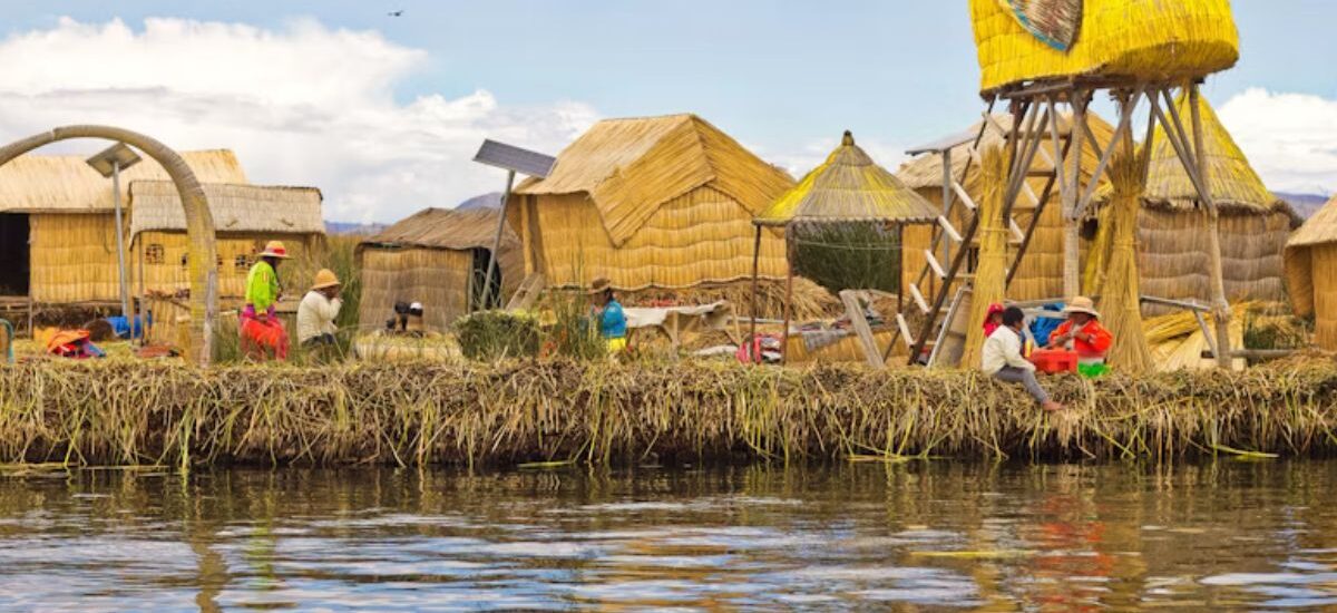 Imagem que mostra comunidade do Lago Titicaca em ilha feita de totora (planta do lago), apresentando crianças próximas a cabanas e embarcação tradicional do lago.