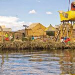 Imagem que mostra comunidade do Lago Titicaca em ilha feita de totora (planta do lago), apresentando crianças próximas a cabanas e embarcação tradicional do lago.