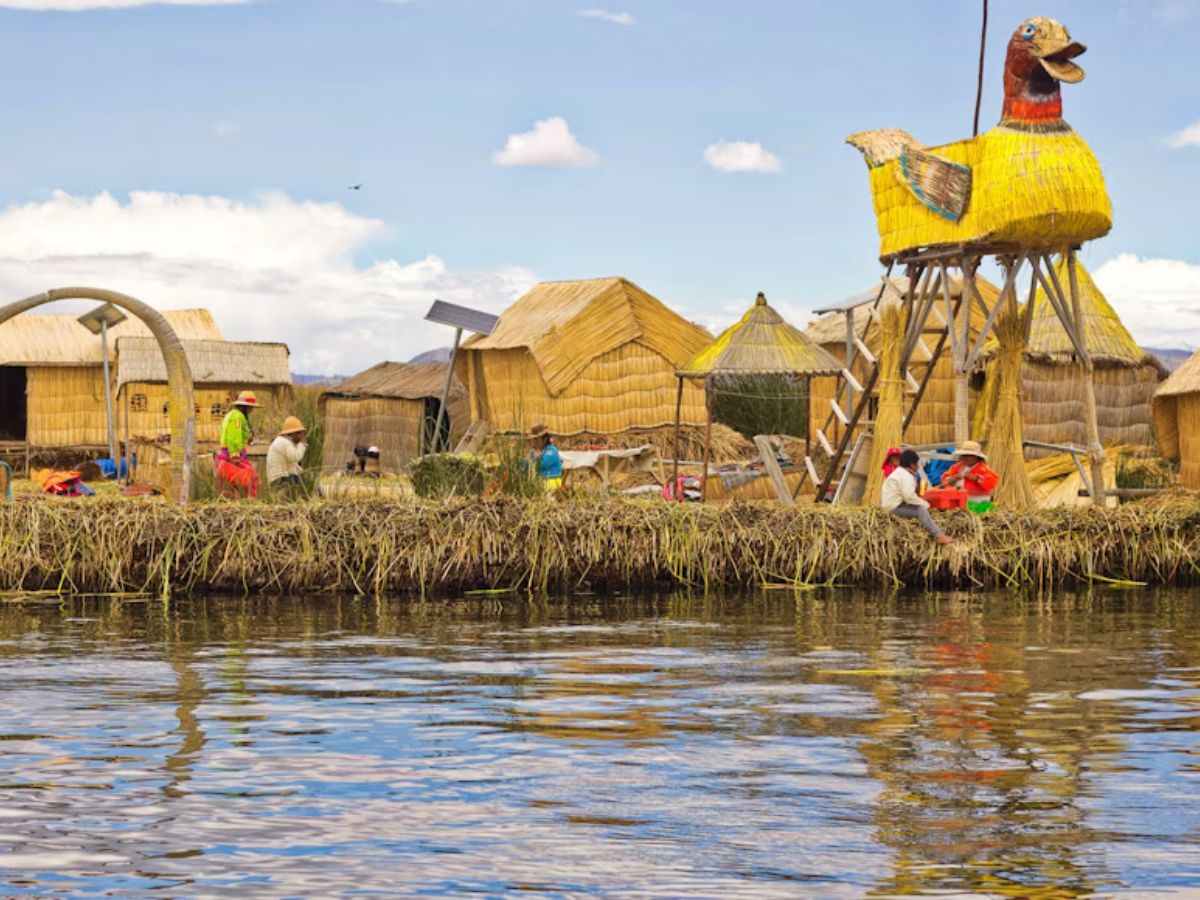 Imagem que mostra comunidade do Lago Titicaca em ilha feita de totora (planta do lago), apresentando crianças próximas a cabanas e embarcação tradicional do lago.